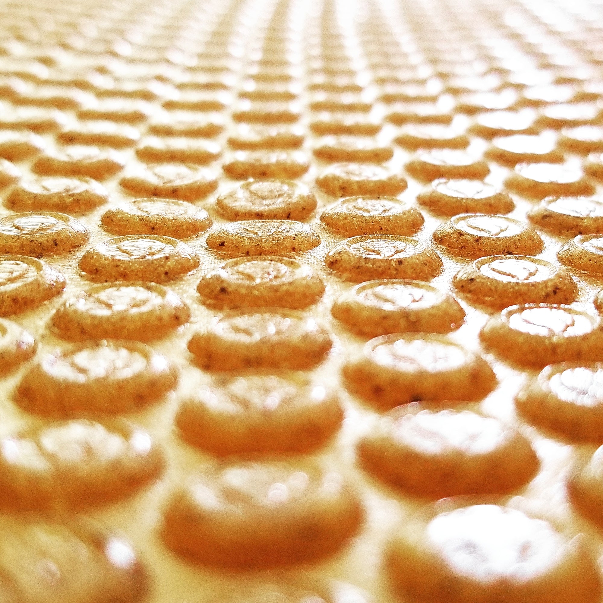 Close-up of freshly made Danger Snacks hard candy pellets in a candy roller sheet, lightly connected by a thin layer of sugar before being separated and packaged.
